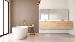 large bathroom with freestanding bathtub, behind it wall panels in brown. Next to it a washbasin with wooden fronts in front of white textured wall panels