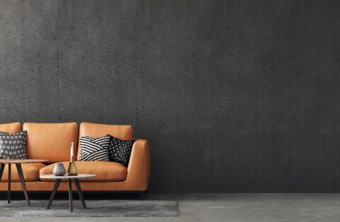 Wandverkleidung im Wohnzimmer mit grauen Strukturplatten im Samt-Look, davor braune Ledercouch mit Zierkissen