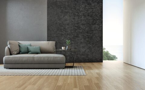 Living room back wall with black textured design panels in creased look, in front of it a small gray sofa and a side table
