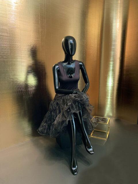 Schaufensterpuppe mit schwarzem Kleid vor goldener strukturierte Designplatte im Shopwindow