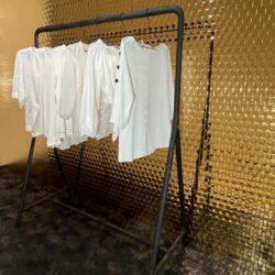 weiße Kleidung auf Kleiderständer im Shopwindow, dahinter spiegelnde strukturierte Designelemente im Rattanlook