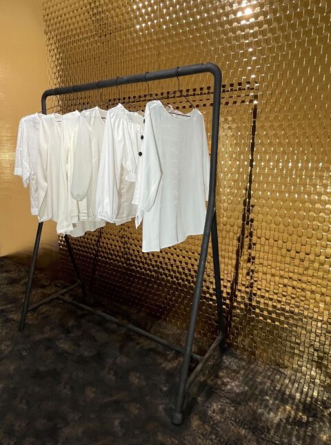 weiße Kleidung auf Kleiderständer im Shopwindow, dahinter spiegelnde strukturierte Designelemente im Rattanlook