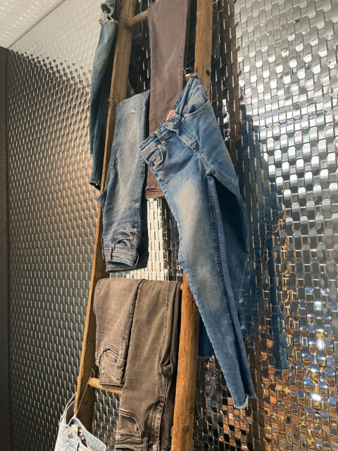 Shopwindow jeans hanging on a ladder with reflective rattan look mirrored textured panel behind it