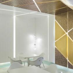 Local with white tables and chairs and a wall with gold patterned decor