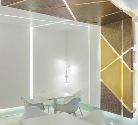 Local with white tables and chairs and a wall with gold patterned decor