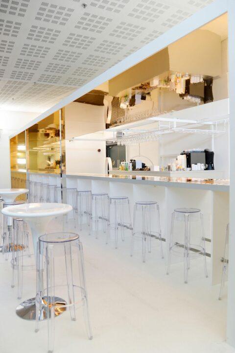 Bar in weiß mit goldenen spiegelnden Elementen und transparenten Barhockern