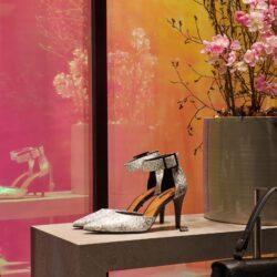 Shopwindow mit Schuhen im Schlangenleder, einem goldenen Blumentopf mit Rosen und im Hintergrund eine schillernde Rückwand in rosa und gelbTönen