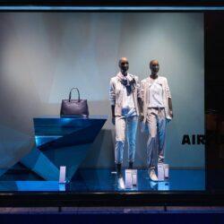 Modernes Shopwindow mit einem futuristischem Produktpräsenter in blau spiegelnd sowie zwei Schaufensterpuppen in heller Kleidung