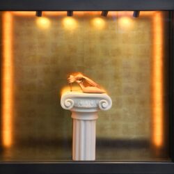 Schaufenster mir einer antiken Säule in der Mitte und einem Schuh darauf, die Rückwand ist mit einem gold gemusterten Dekor verkleidet