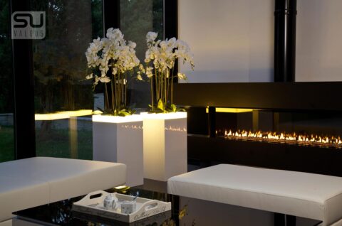 Sitzecke in beige vor einem Kamin davor weiße hochglänzende Podeste mir Orchideen