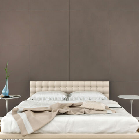 Bed with light bedding in front of brown wall with square pattern