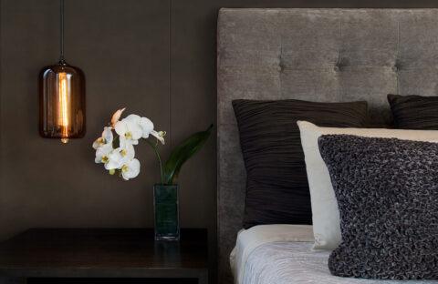 Detail of gray bed back wall next to brown wall, on the nightstand is an orchid