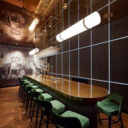 Bar with dark paneled walls and green bar stools around a large wooden table