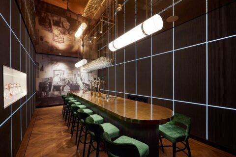Bar with dark paneled walls and green bar stools around a large wooden table