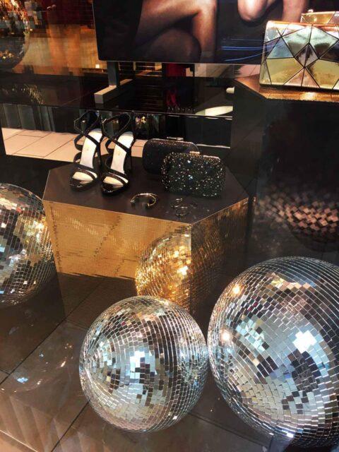 Schaufenster mit goldenen und silbernen Diskokugeln, Sandalen und Handtaschen aus einem Mosaikpodest