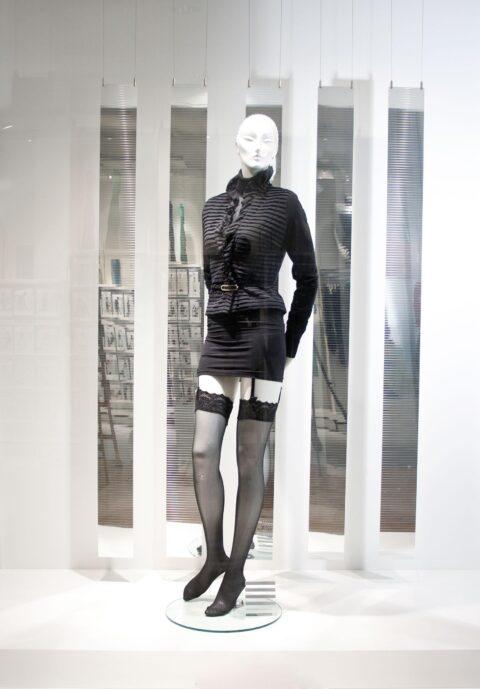 Schaufenster mit einer Schaufensterpuppe, im Hintergrund hängen silberne Elemente im Mosaiklook