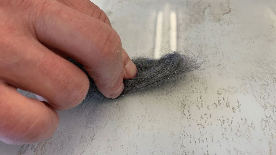 Hand, die mit Stahlwolle über eine helle Glasplatte reibt