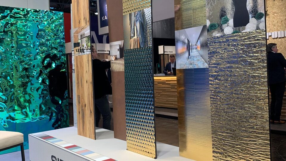 Exhibition stand Euroshop, pedestal on the floor in beige, in it there are six differently pasted panels. Panels in wood look, steel look, rattan look and structured mirror look. With sample photos of applications.