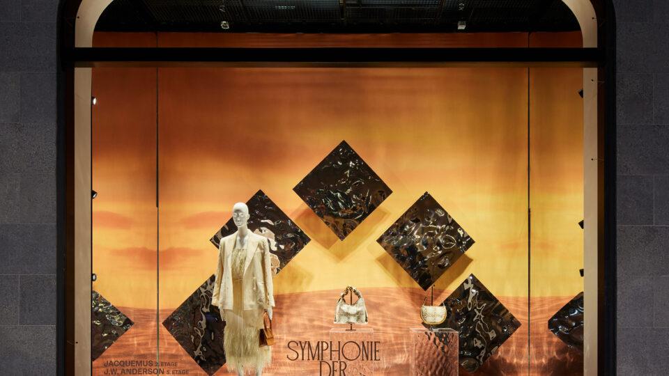 Schaufenster, Hintergund orange mit Sonnenuntergangsstimmung, die Schaufensterpuppe mit weißem Kopf trägt weiße Kleidung. Hauptfarbe des Schaufensters ist orange.