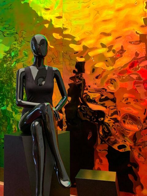 Schwarze Schaufensterpuppe vor schillernden Grün- und Orangetönen