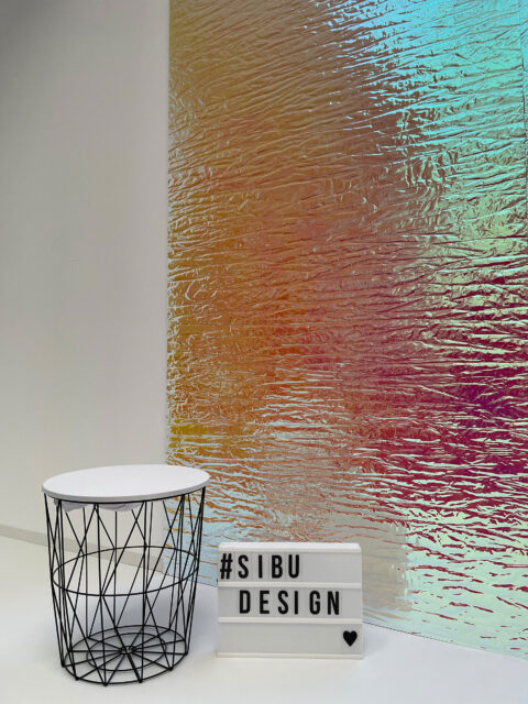 schwarzer moderner Hocker vor schillernden Rosa- Gelbtönen