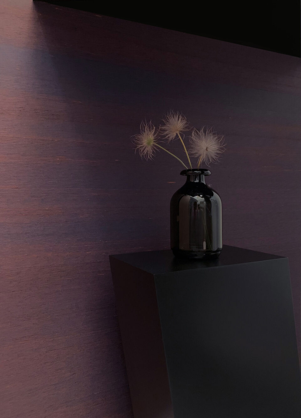 schwarze Vase mit hellen Pflanzen vor violettem Hintergrund