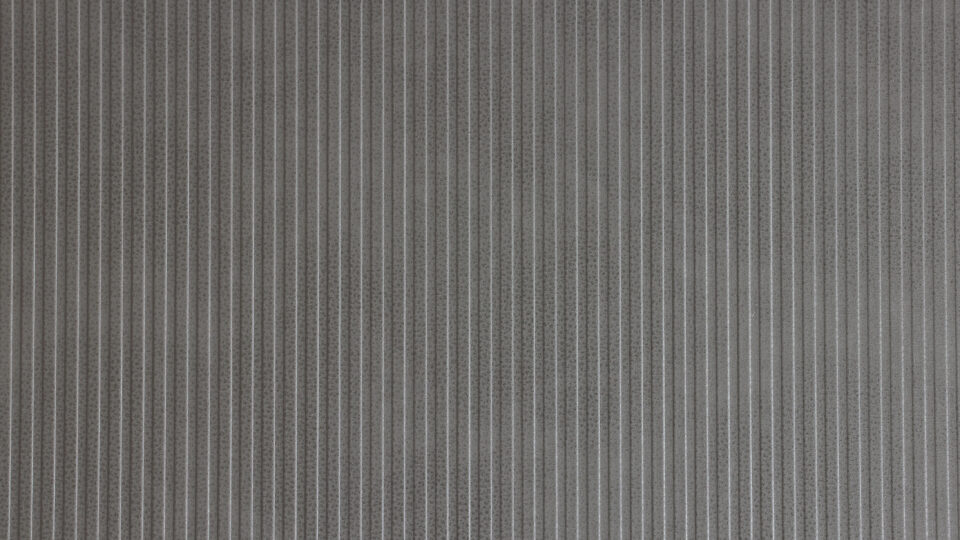 Detailaufnahme einer Dekorplatte dessen Design eine strukturierte vertikale Linienführung zeigt. Edle schmale Streifen, die sowohl in den Höhen als auch in den Tiefen gleichmäßig sind. Die Oberfläche stellt ein genarbtes hellgraues Leder dar.