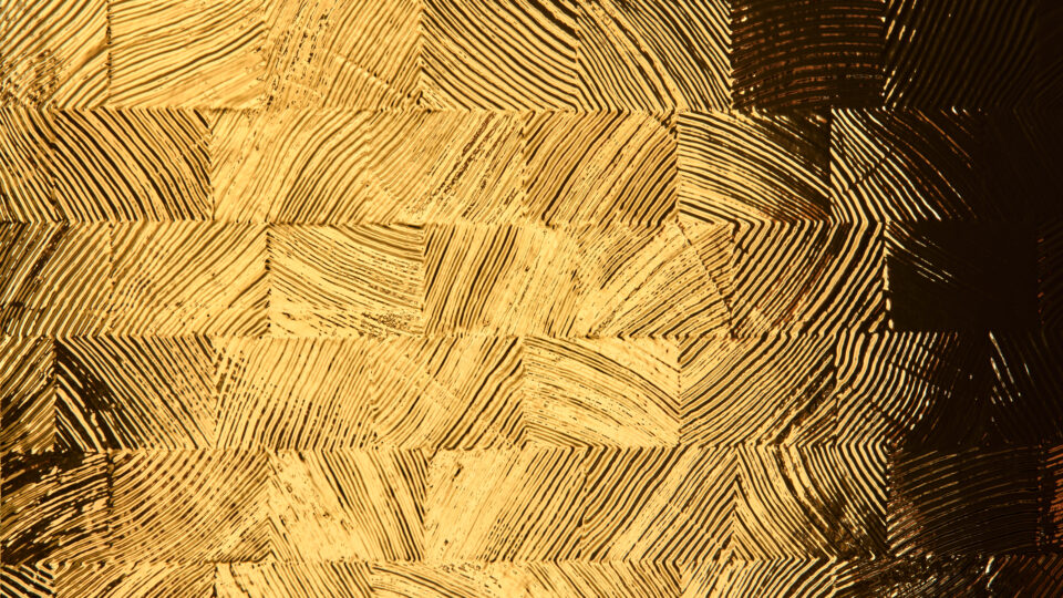 Detailaufnahme eines Designpaneels, dessen Struktur Holzmosaiken ähnelt. Das Oberflächenmaterial des Designs ist spiegelnd wodurch die Licht Reflektionen die Struktur besonders gut zur Geltung bringen. Die Farbe des strukturierten Spiegels ist Gold.