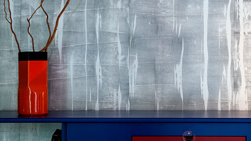 moderne farbenfrohe Kommode in blau rot und gelb vor grauer effektvoller Wandverkleidung