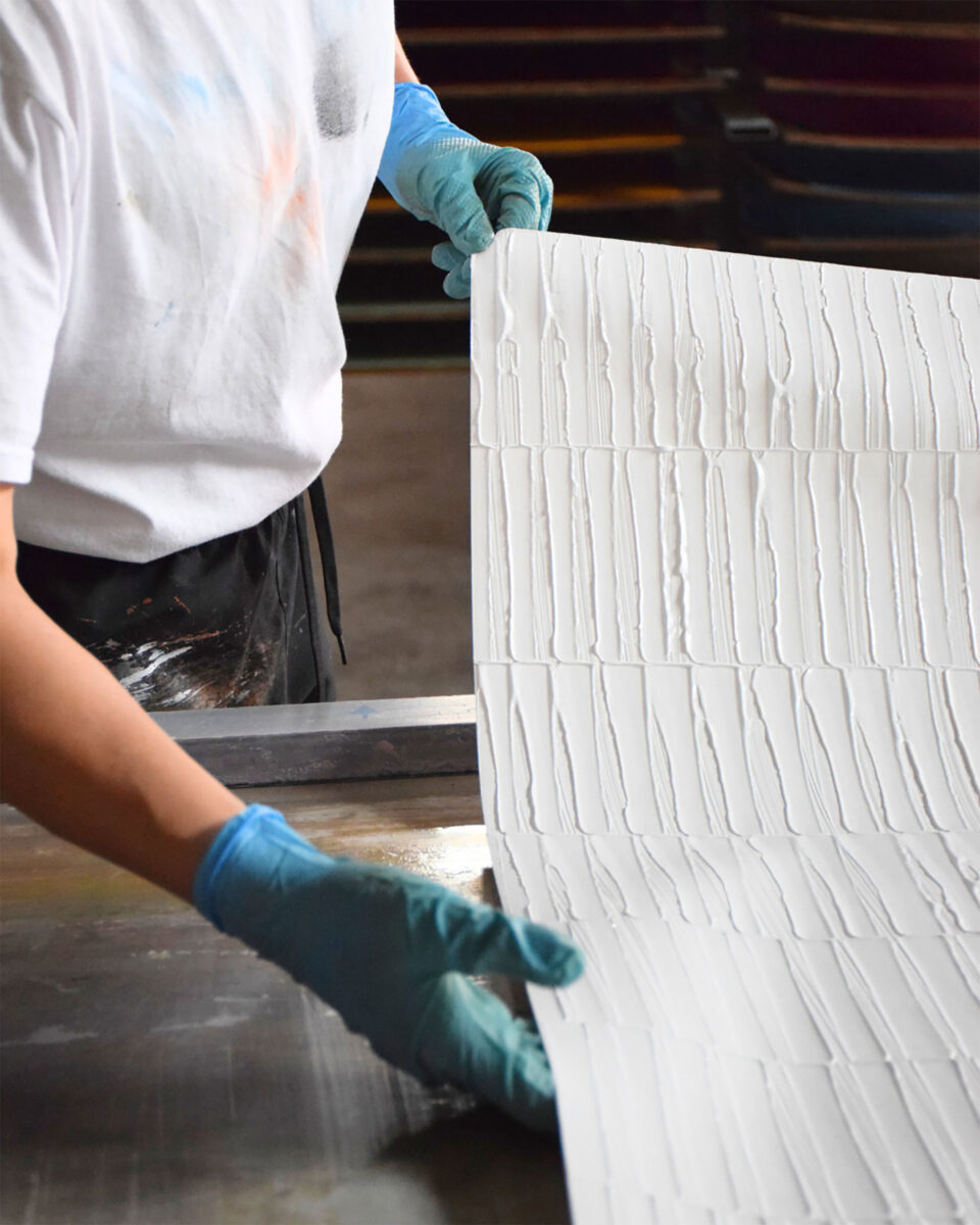 händische Fertigung der Artmura-Wandbeläge - Produktionsmitarbeiter zeigt strukturierten Bogen her.