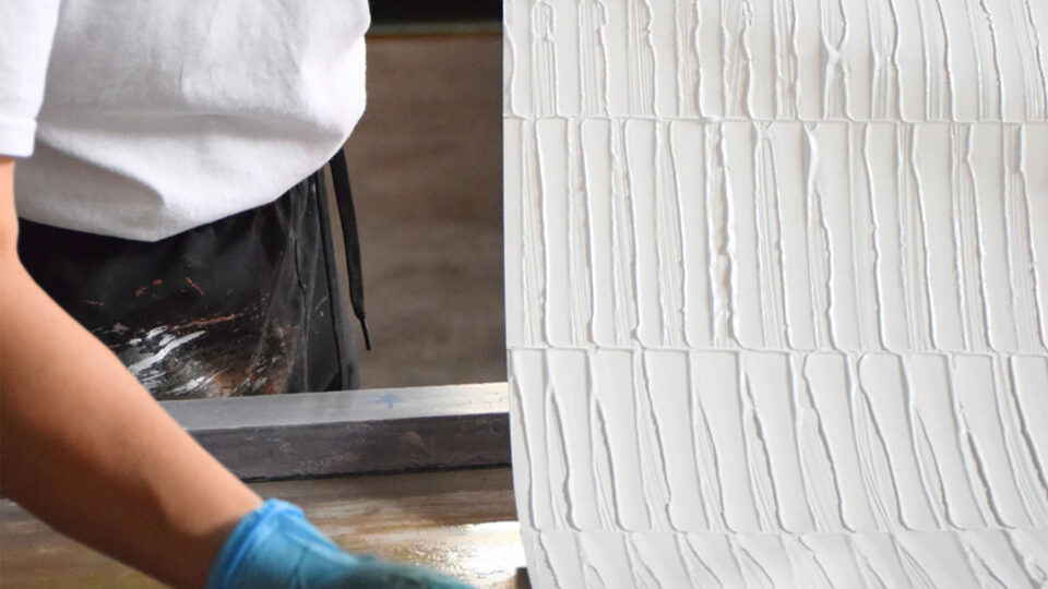 händische Fertigung der Artmura-Wandbeläge - Produktionsmitarbeiter zeigt strukturierten Bogen her.