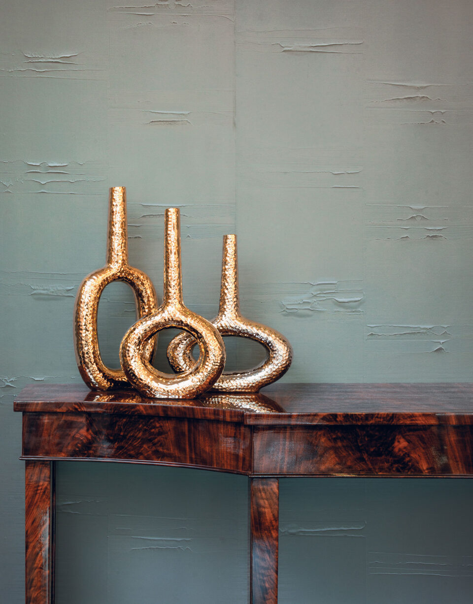 Beistelltisch mit goldenen Vasen vor einer modernen grauen Wand mit strukturierten Wandbelägen