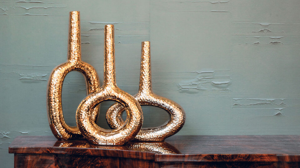 Beistelltisch mit goldenen Vasen vor einer modernen grauen Wand mit strukturierten Wandbelägen