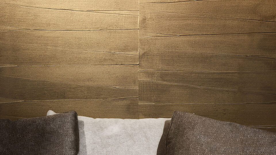 Ausschnitt einer flauschigen Couch vor einer goldenen strukturierten Wandgestaltung in Bronzetönen