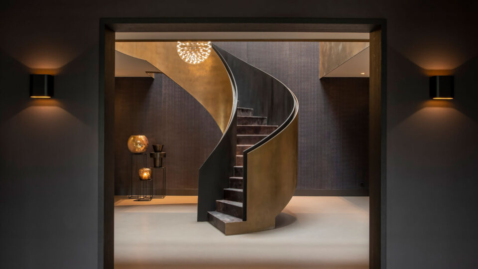 Ein moderner Stiegenaufgang in mitten einem Raum - dunklen Farben gepaart mit goldenen Akzenten dargestellt durch hochwertige Wandbeläge