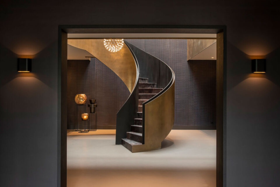 Ein moderner Stiegenaufgang in mitten einem Raum - dunklen Farben gepaart mit goldenen Akzenten dargestellt durch hochwertige Wandbeläge