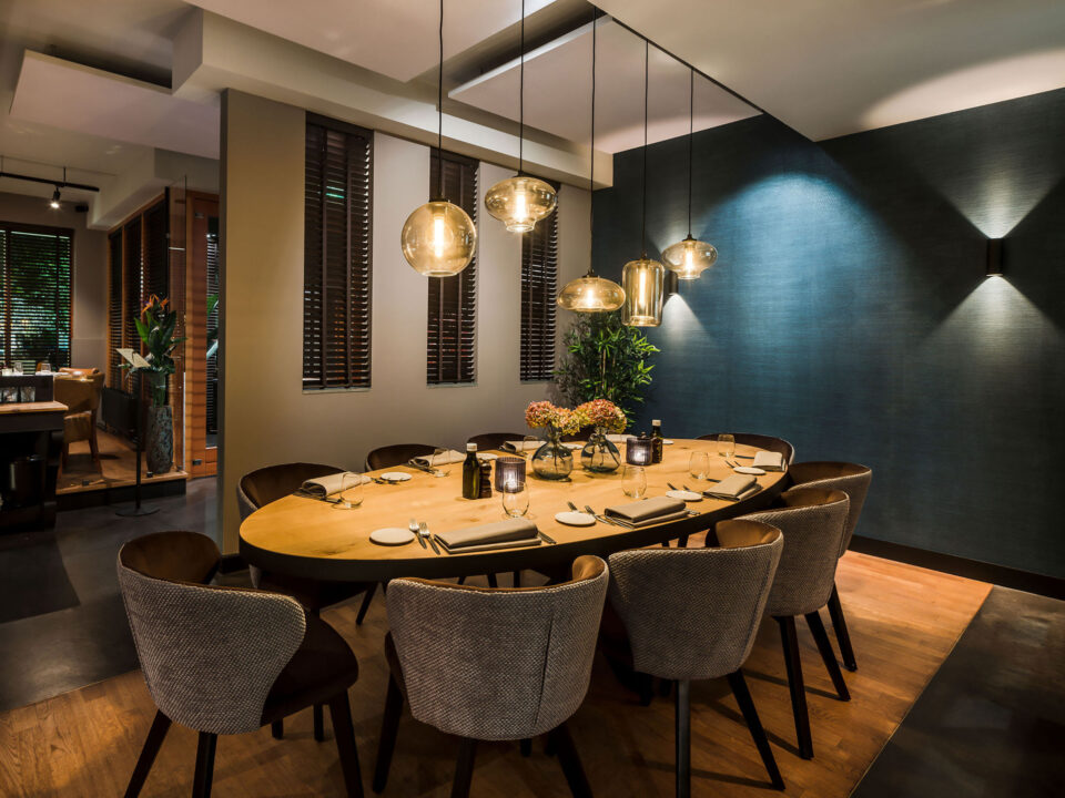 Gemütlich aber modern gestalteter Essbereich. Ein liebevoll gedeckter Tisch, moderne Lampen die in verschiedenen Formen den Tisch ausleuchten, Dahinter eine farbige Tapete in Petrolblautönen die den Raum mit Farbe füllt.