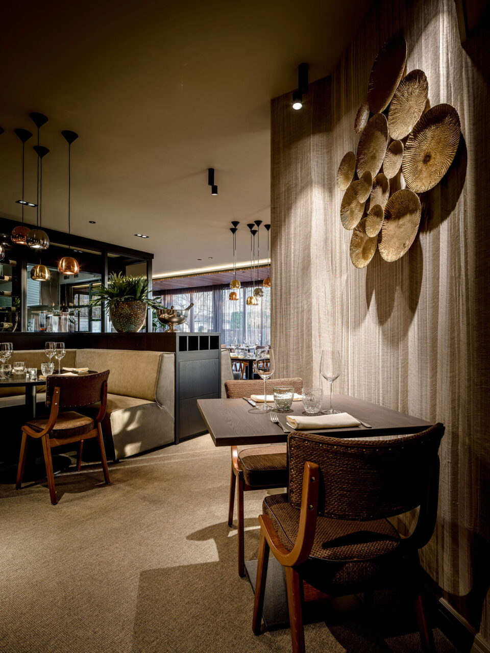 Ein Restaurantbereich mit kleinen gemütlichen Tischen. Die Wand wird durch eine Tapete geschmückt die in vertikalen Linien verläuft.