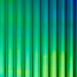 A close-up of a design panel, characterized by wide vertically running lines. The surface is reflective, with a color that shifts from green to blue depending on the viewing angle. The varying heights and depths of the structure create a particularly deep effect that captivates.