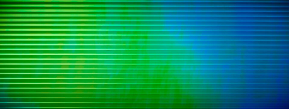 Shown is a photo of a decorative panel. The design features linear patterns, and the surface material is reflective and shifts in color - from green to blue - depending on the viewing angle.