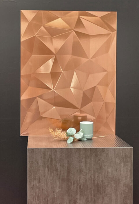 SIBU DESIGN cup with a leaf and shrub in front of a design panel with a diamond-like structure, copper colored and shiny, reflective surface.