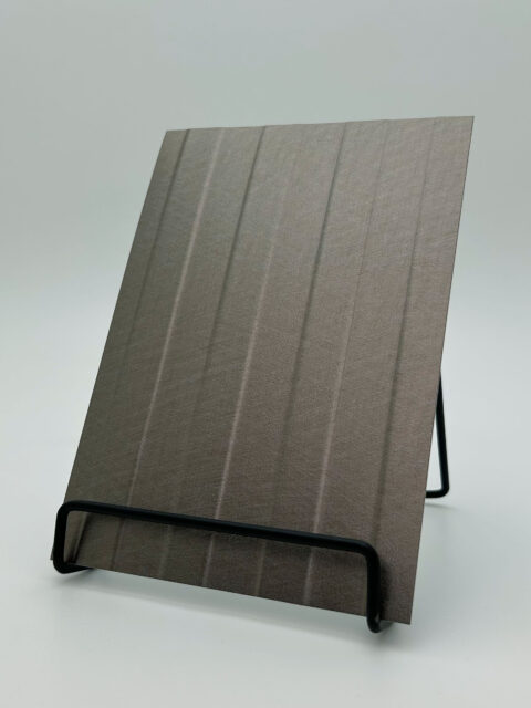 Display stand with a gray metallic design panel made of faux leather. The structure features vertical lines that are both recessed and raised.