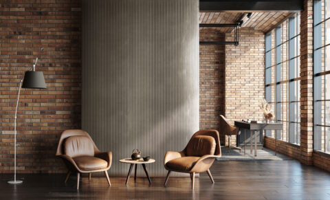 Brown, comfortable chairs with a small table and a teapot on them. In the background, a gray metallic design panel made of faux leather. The structure features vertical lines that are both recessed and raised.