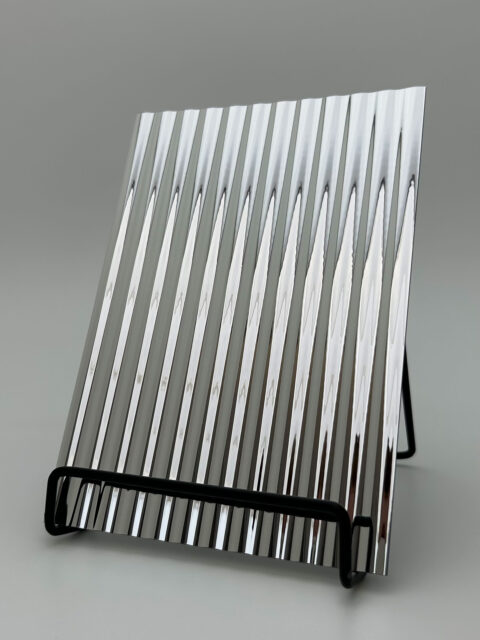 Display stand with a reflective, silver design panel whose structure is characterized by wide vertical lines.