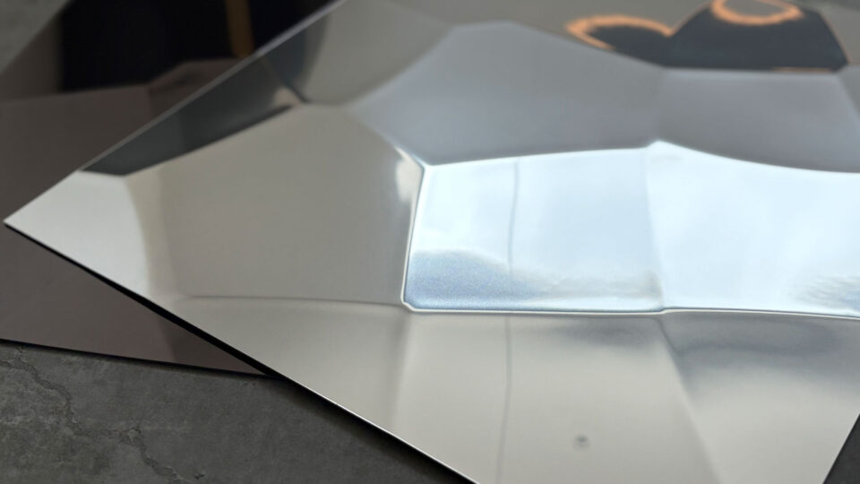 Shown are color variants of the SL FACET wall panel in reflective silver and anthracite. The structure resembles repeatedly folded sheet metal.