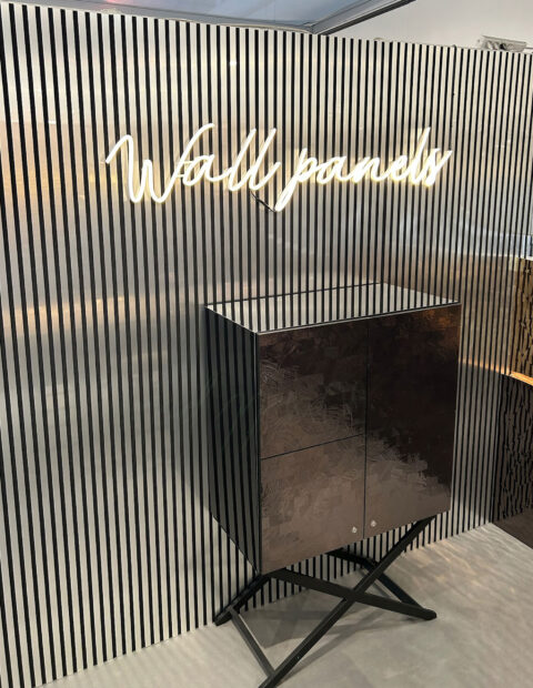 Wand verkleidet mit Akustikpaneel- Optik: Silber gebürstete Streifen vor schwarzem Untergrund, Davor eine Leuchtreklame mit dem Schriftzug 