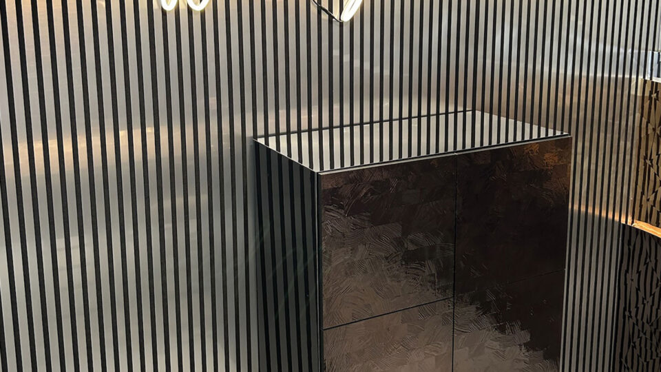 Wall covered with acoustic paneling – design: silver brushed stripes against a black background. In front of it, an illuminated sign with the word 