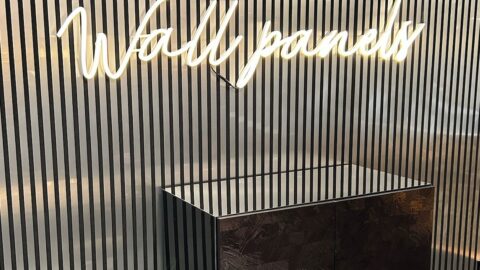 Wall covered with acoustic paneling – design: silver brushed stripes against a black background. In front of it, an illuminated sign with the word 